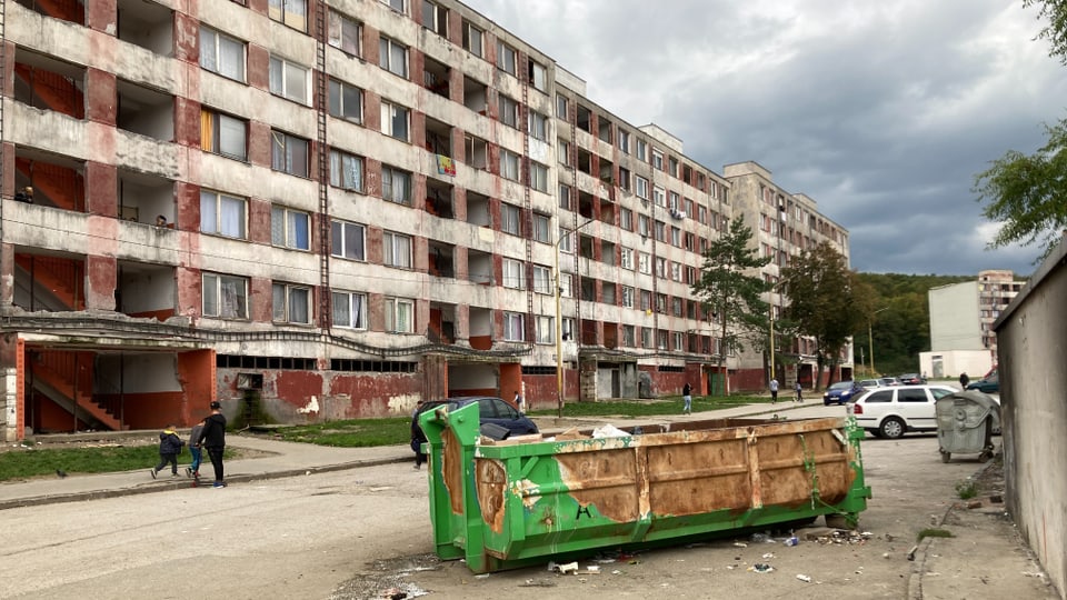 Eine Abfallmulde vor dem heruntergekommenen Plattenbau.