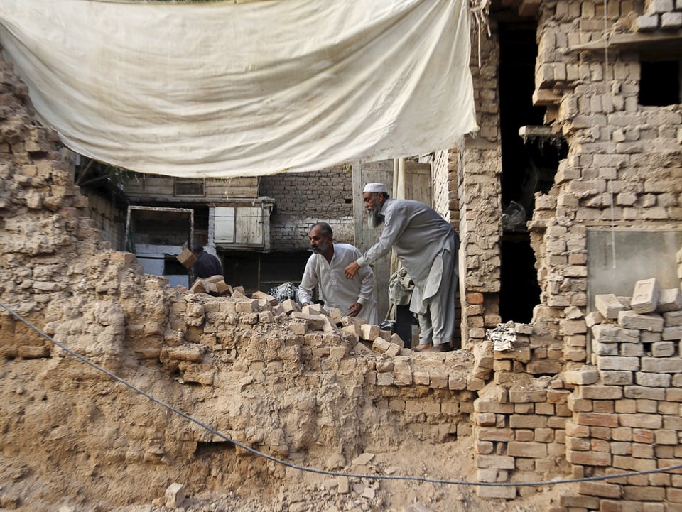 Männer stehen vor einem zerstörten Haus