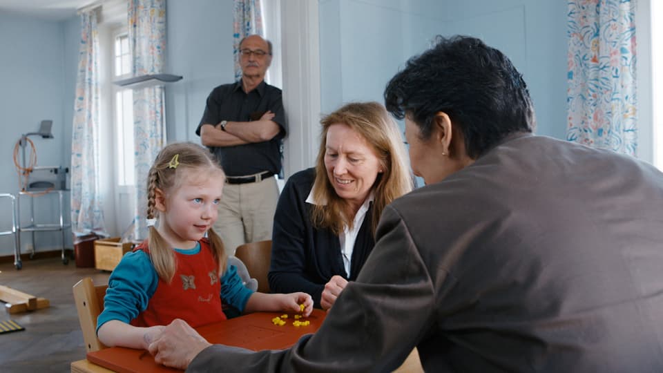 Mara macht eine Übung, bei der sie nur eine Hand benutzen darf, im Hintergrund Remo Largo (Abteilung Entwicklungspädiatrie Kinderspital Zürich)