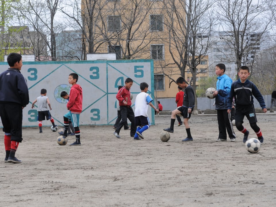 Jugendliche beim Fuassballspiel auf einem Hartplatz.