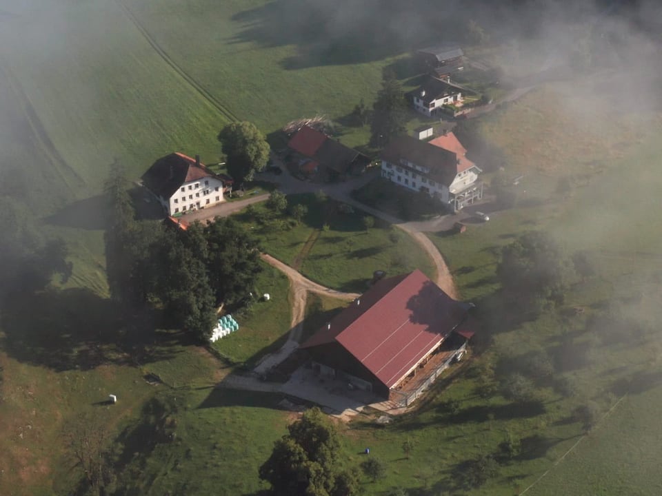 Luftaufnahme eines nebligen Bauernhofs mit Gebäuden und Feldern.