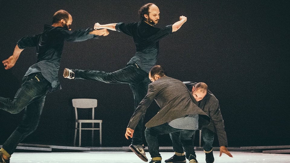 Bühnenbild: Vier dunkel gekleidete Tänzer, der eine scheint zu fliegen.