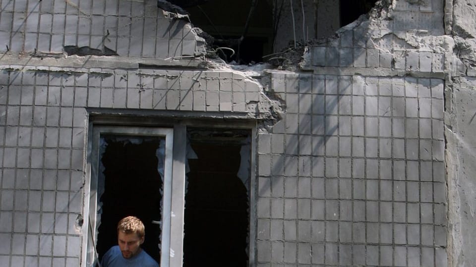 Mann schaut aus dem Fenster eines beschädigten Wohnhauses in Donezk