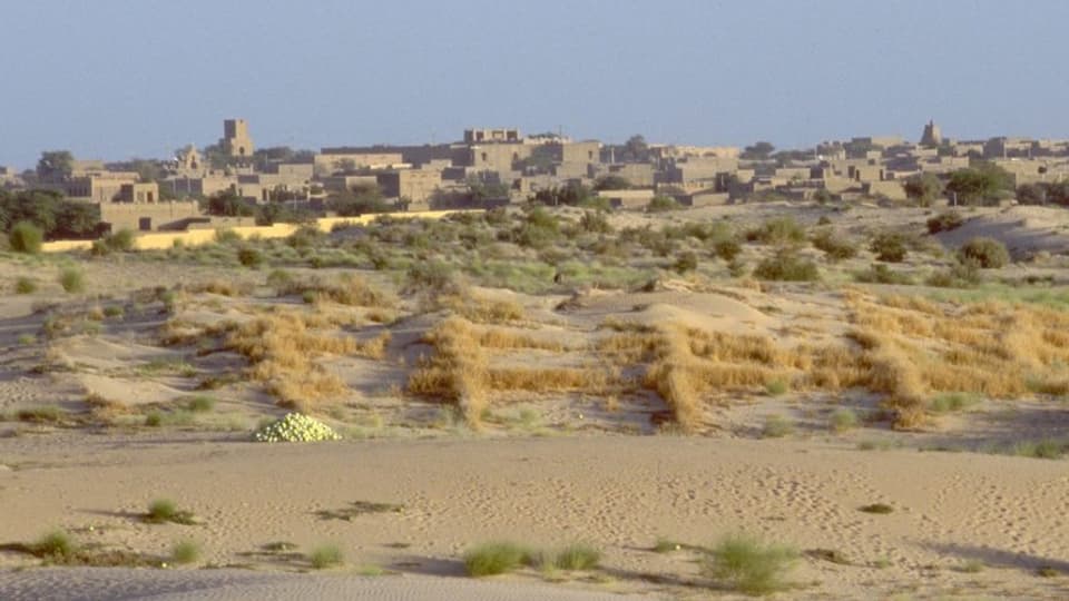 Lehmgebäude und die Wüste Sahara im Vordergrund.