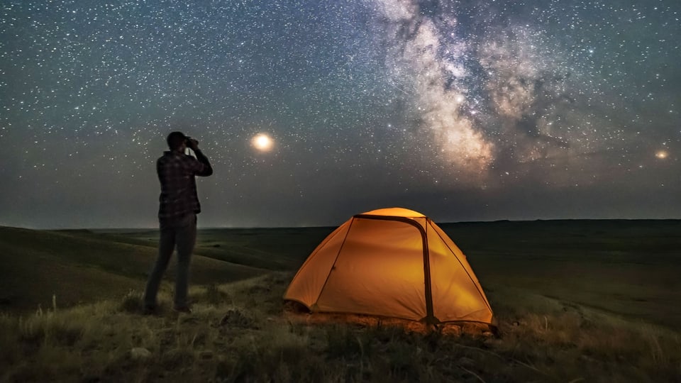 Ein Mann steht neben einem Zelt und schaut auf den klaren Sternenhimmel. 