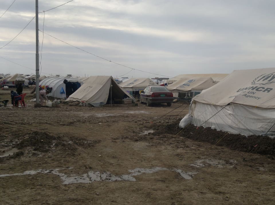 Matschiger, nasser Boden im Flüchtlingslager. Dahinter Zelte.