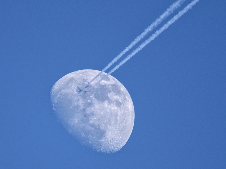 Blauer Himmel, Mond und Flugzeug mit Kondesstreifen