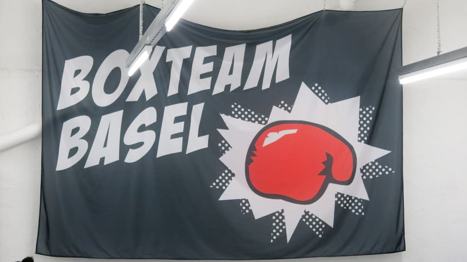 Eine Flagge mit dem Emblem vom Boxclub und dem Schriftzug hängt an einer Wand.