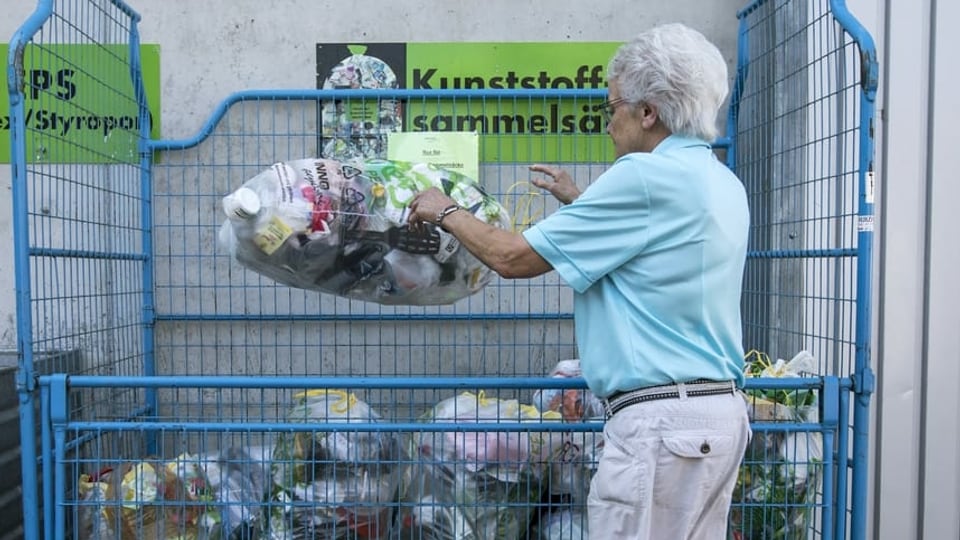 Frau legt Sack mit Plastikabfällen in einen Gitterkasten