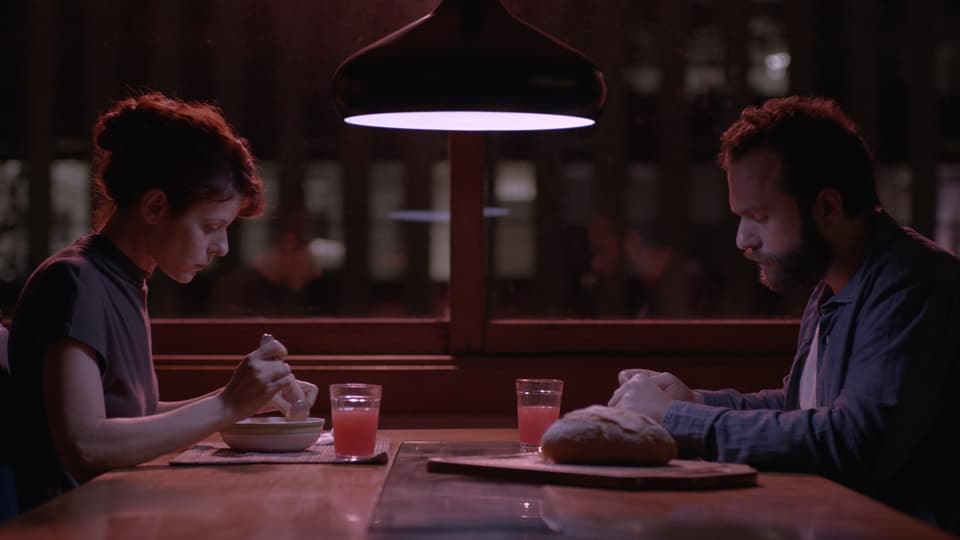 Eine Frau und ein Mann sitzen an einem Tisch und essen. Sie schauen sich nicht an.