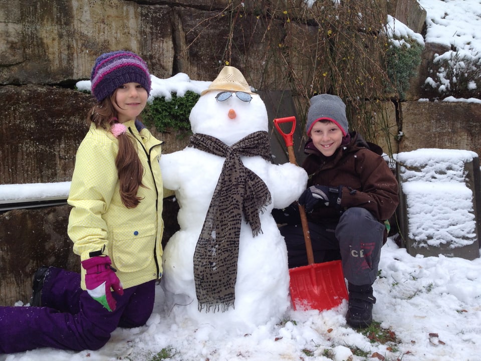 Links des Schneemanns ein Mädchen, rechts davon ein Knabe.