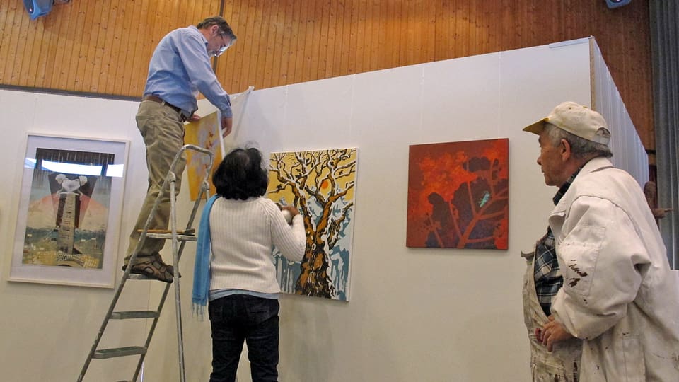 Ein Mann auf einer Leiter und eine Frau am Boden hängen Gemälde auf.