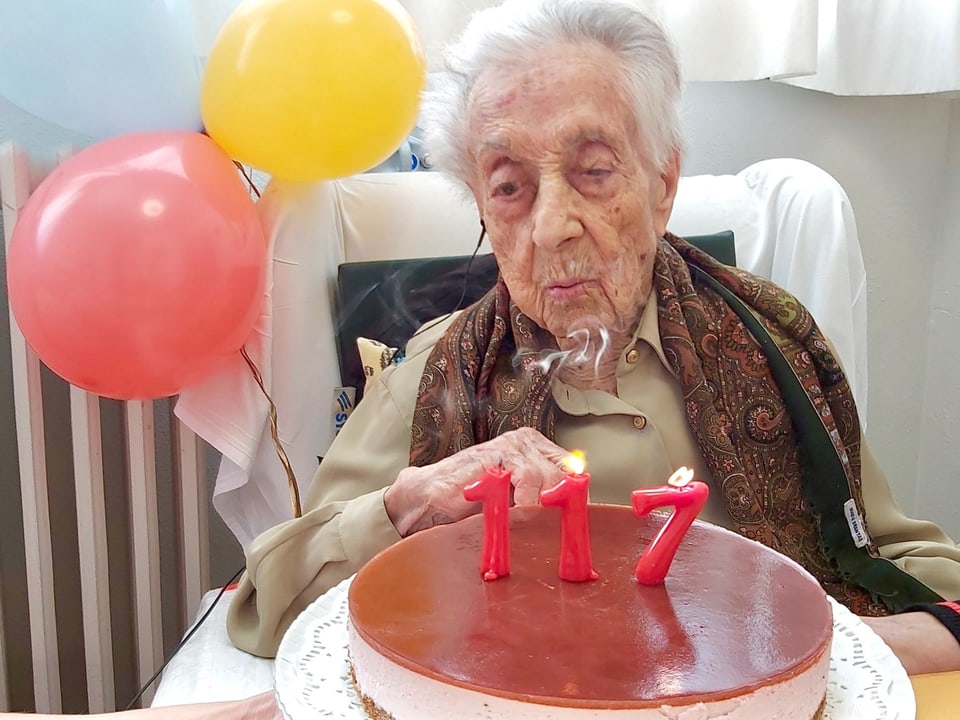 Idoso soprando velas de aniversário em um bolo com o número 117.