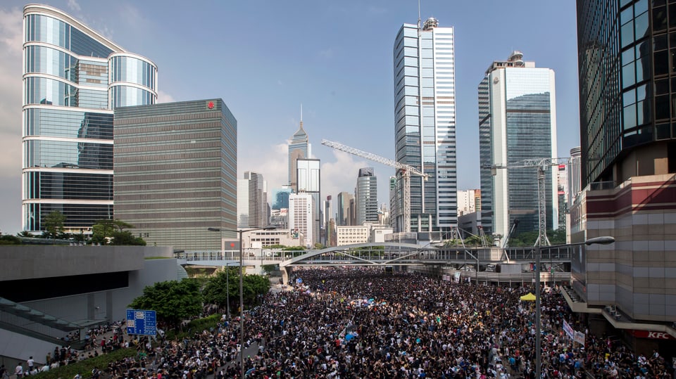 Mit Menschen gefüllte Strasse im Finanzdistrikt von Hongkong, im Hintergrund Bürogebäude, Hochhäuser.