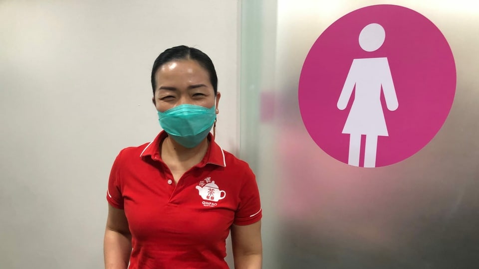 Frau mit rotem Poloshirt vor Toilettentür