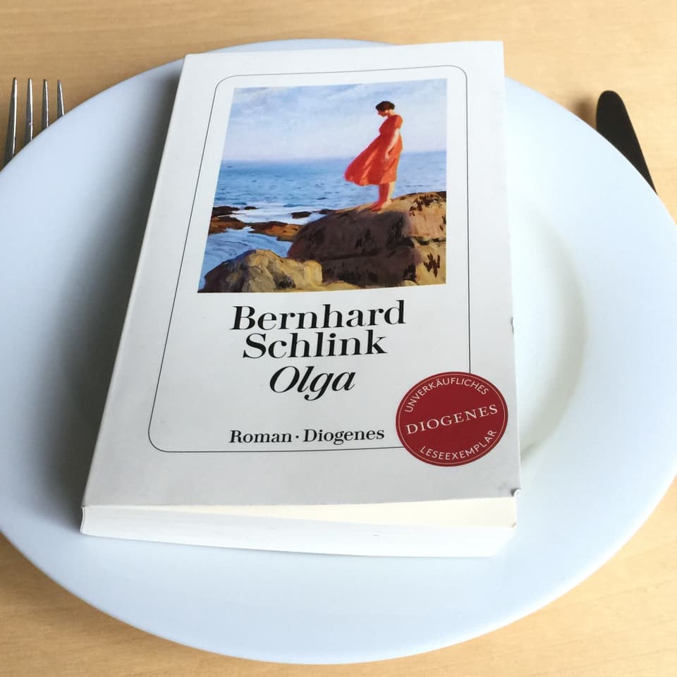 Der Roman «Olga» von Bernhard Schlink liegt auf einem weissen Teller, Messer und Gabel daneben.