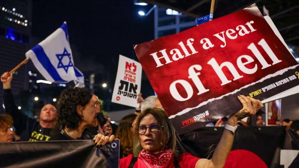 Menschen demonstrieren in Tel Aviv, eine Frau hält ein Schild mit den Worten «Half a year of hell».