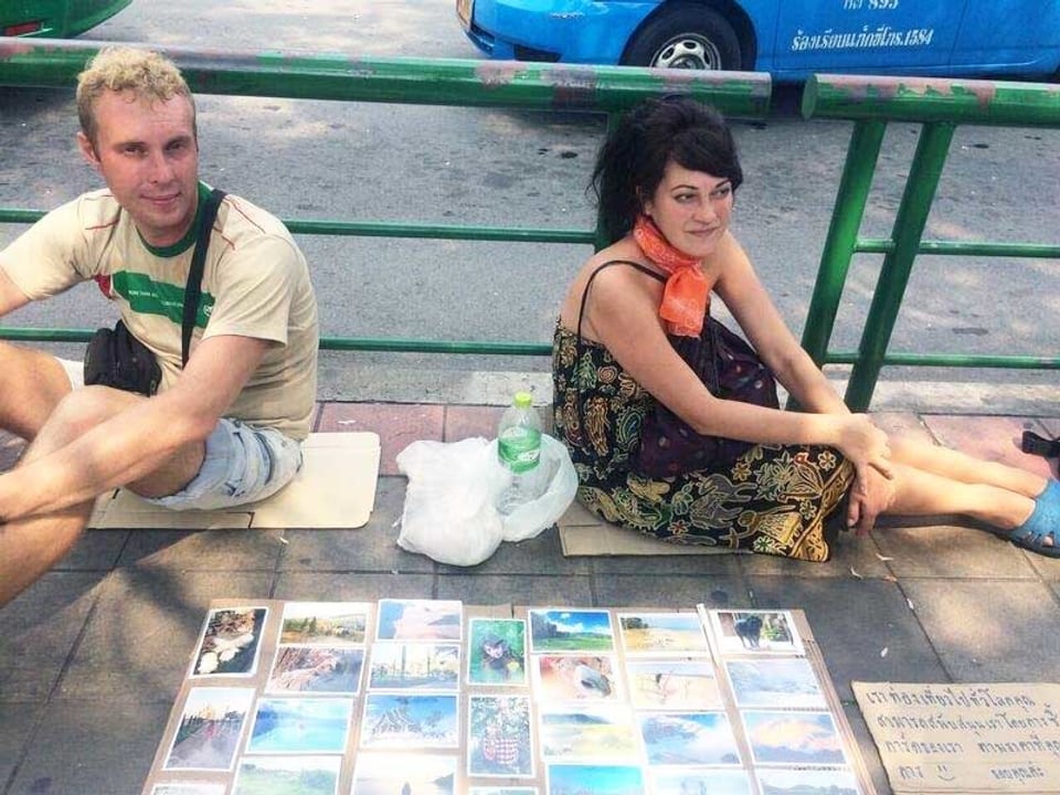 Zwei junge Leute sitzen auf dem Boden auf der Strasse und verkaufen Postkarten.