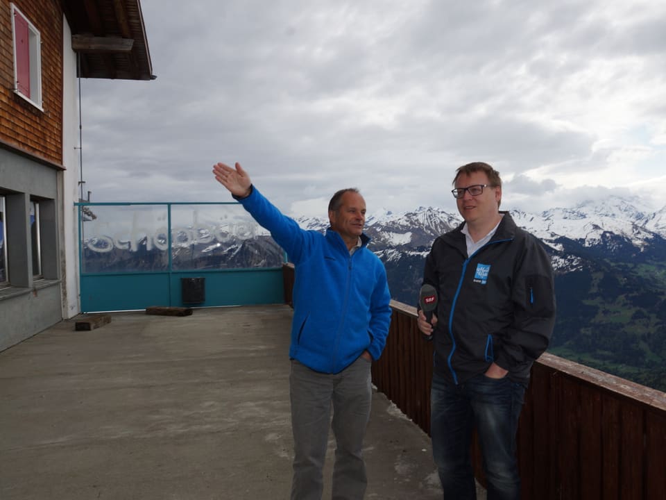 Zwei Männer auf einer grossen Terrasse von einem Berghaus.