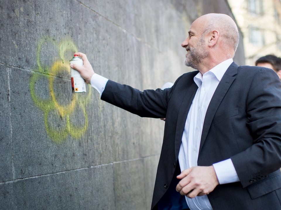 Ein Mann in Anzug besprüht mit einer Dose eine Wand.