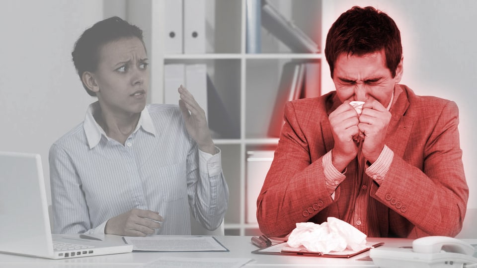Büroszene: Kranker Mann schneuzt sich die Nase, während sich eine Arbeitskollegin entsetzt abwendet