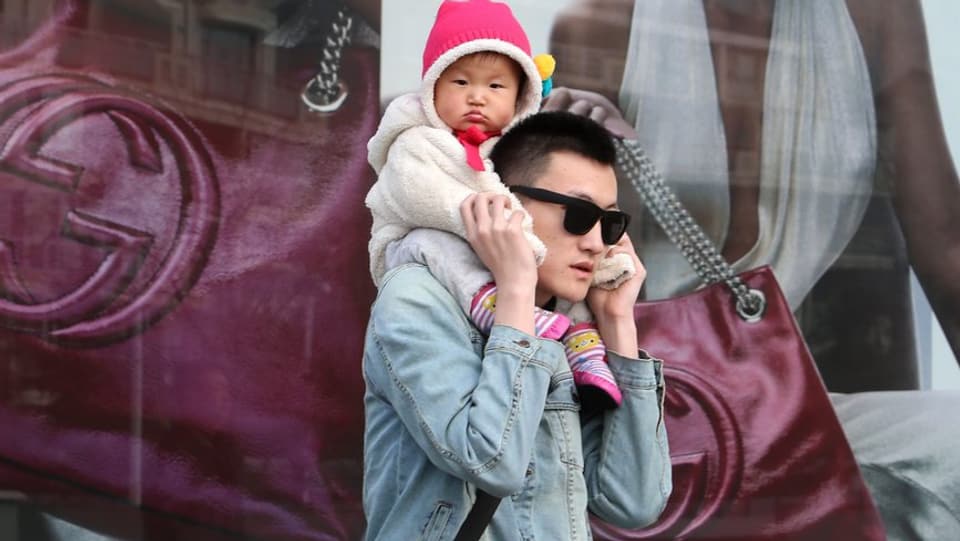 Ein Chinese mit einem Baby auf den Schultern vor einem Gucci-Plakat.