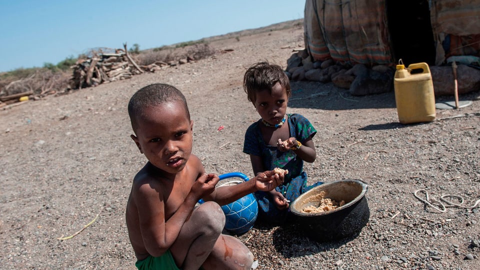 Schwarze Kinder im afrikanichen Niemandsland essen aus einem Topf.