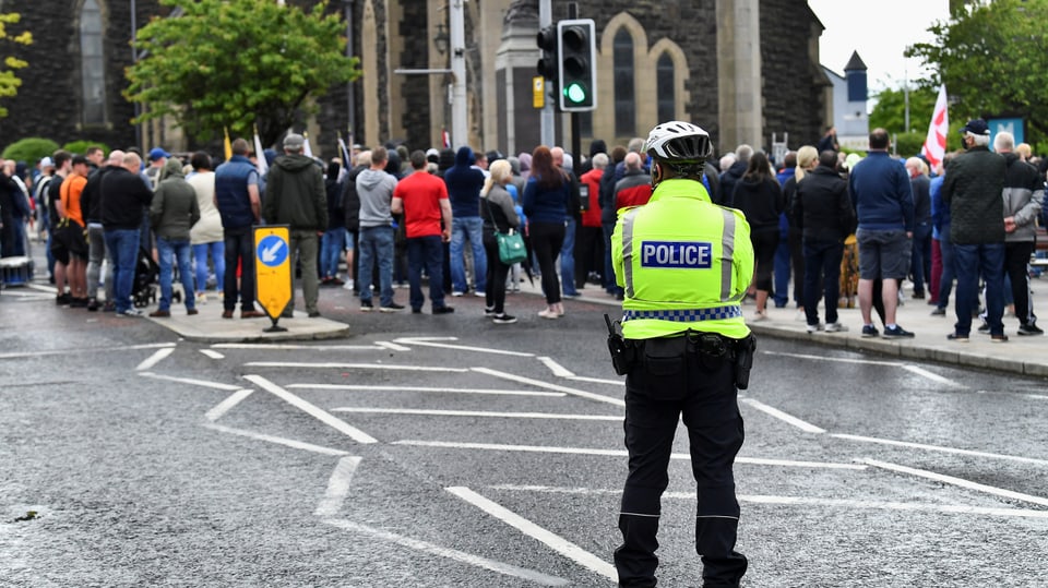 Polizeibeamter in gelber Schutzweste blickt auf Menschenmenge auf Strasse