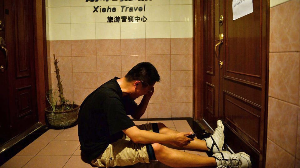 Ein Mann sitzt vor einer verschlossener Tür weinend am Boden
