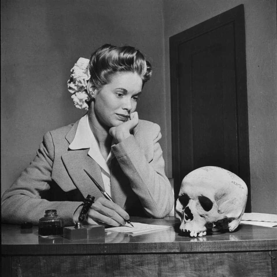 Eine Frau sitzt am Schreibtisch und schaut auf einen Totenkopf.