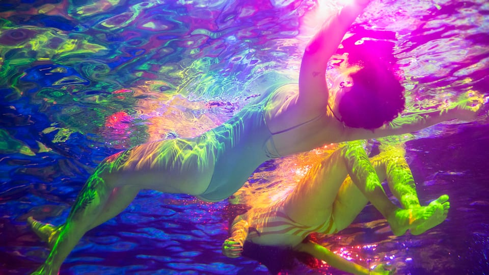 Unterwasseraufnahme einer schwimmenden Frau in einem farbig beleuchteten Schwimmbad