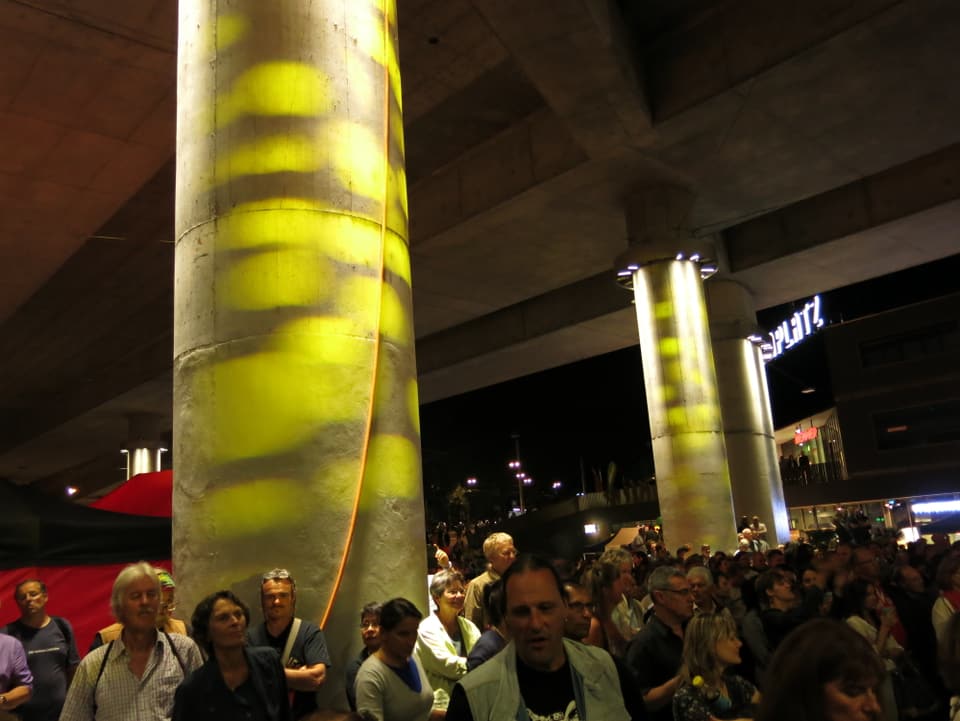 Gelb beleuchtete Säule der Autobahnbrücke am Europaplatz, viel Publikum.