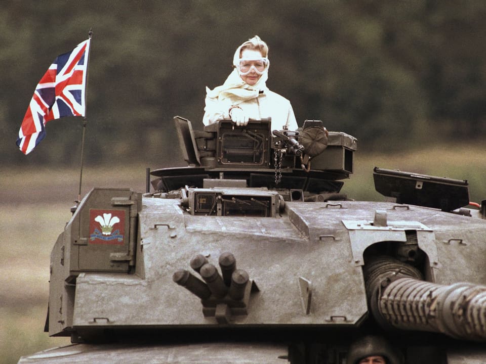 Margaret Thatcher sitzt mit Schutzbrille und Kopftuch in einem Panzer.