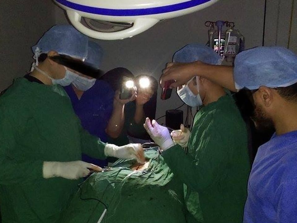 Während einer Operation leuchten zwei Operationsassistenten mit dem Handy