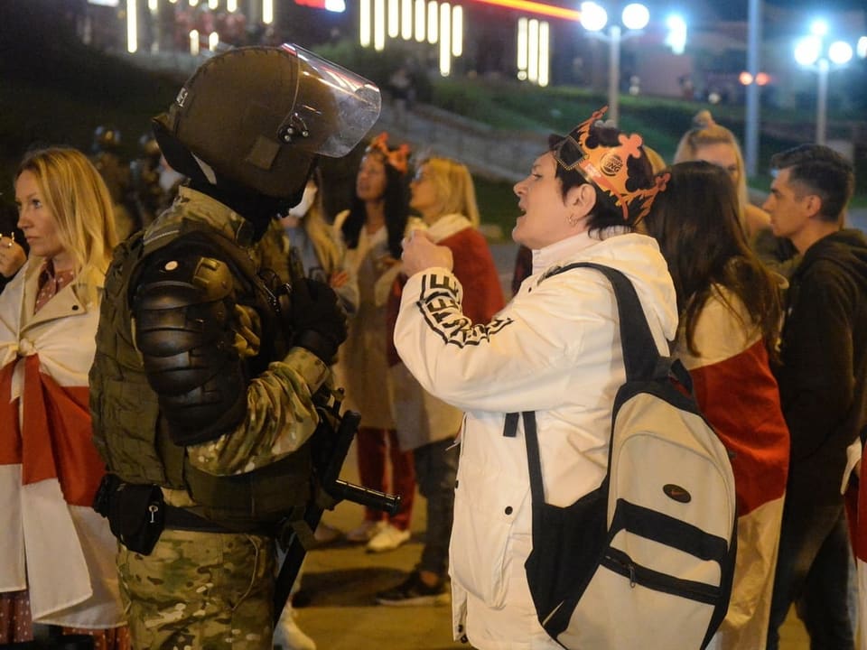 Eine Protestierende spricht mit einem maskierten Polizisten.