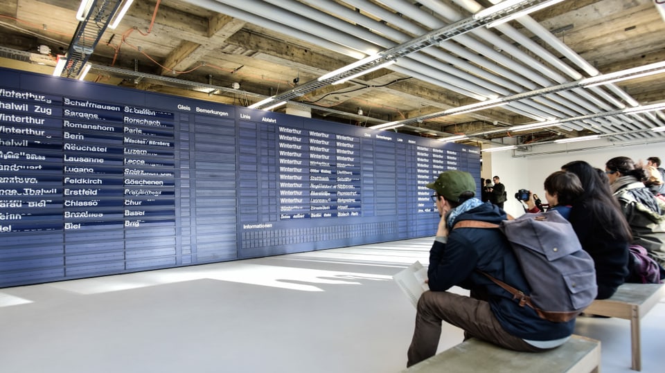 Besucherinnen und Besucher betrachten im MuDA die ausrangiert Fallblattanzeige des Zürcher Hauptbahnhofs