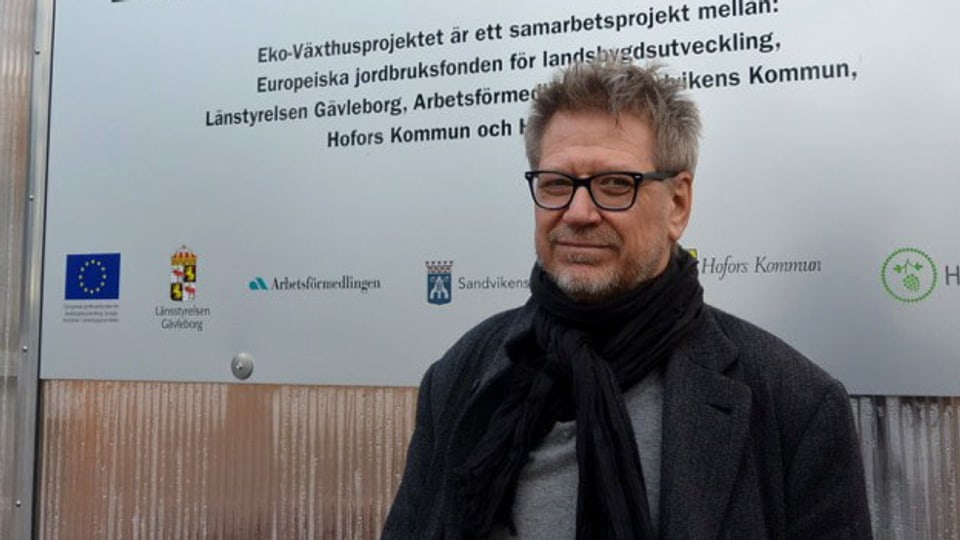 Ein Mann mit Brille steht vor einer Tafel mit der Aufschrift "Eko Växthusprojektet"