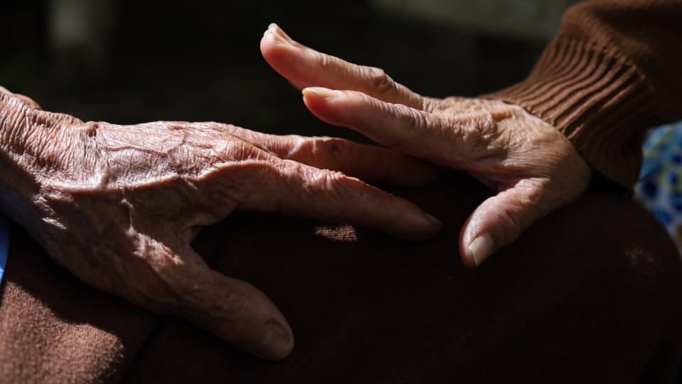 Eine ältere Frau streichelt die Hand eines älteren Mannes