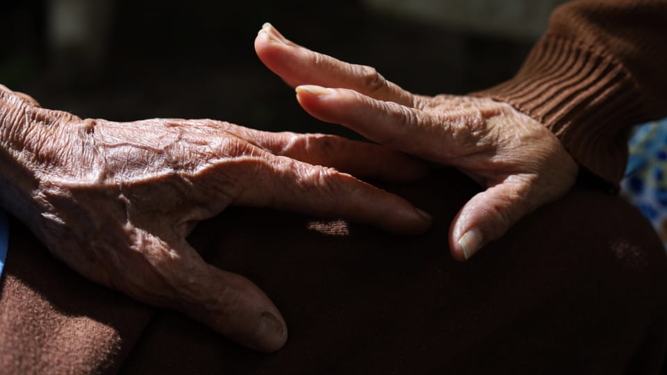 Eine ältere Frau streichelt die Hand eines älteren Mannes