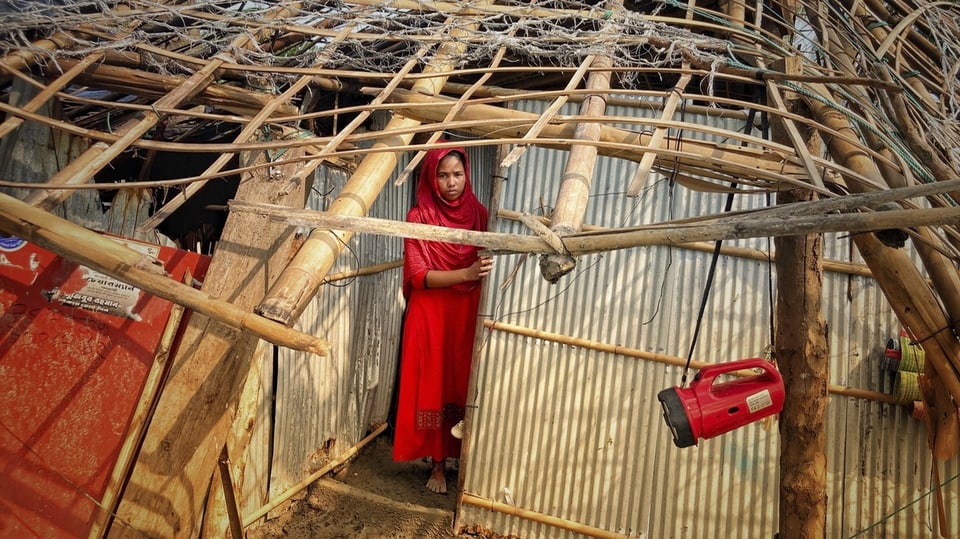 Eine Frau steht an der Tür zu einem Bambus- und Blechhaus, bei dem das Dach fehlt