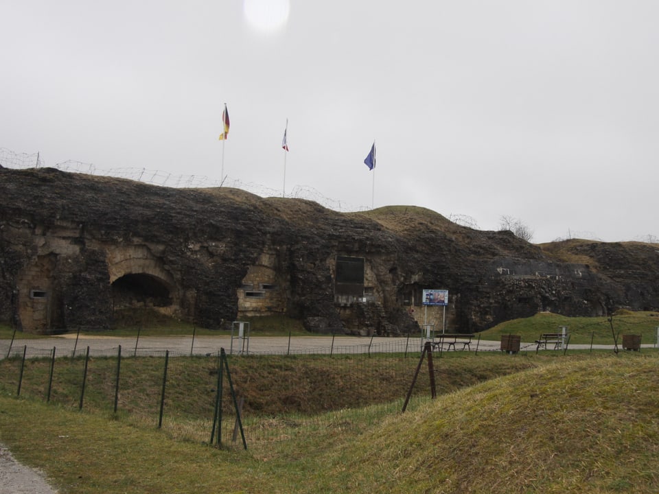 Bewachsene Überreste eines steinerne Fort, auf dem die deutsche, französische und europäische Fahne wehen.