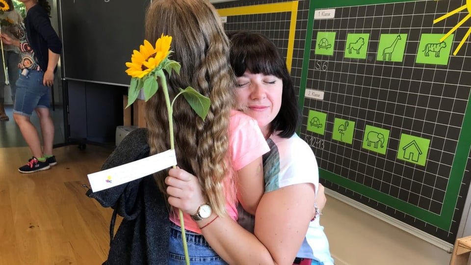 Mutter Alona umarmt ihre Tochter und hält eine Sonnenblume in der Hand.