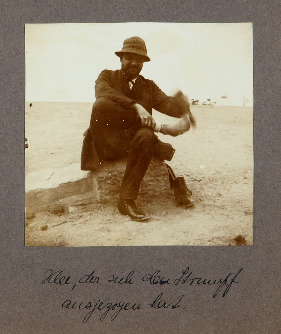 Mann sitzt in Wüste auf Stein.