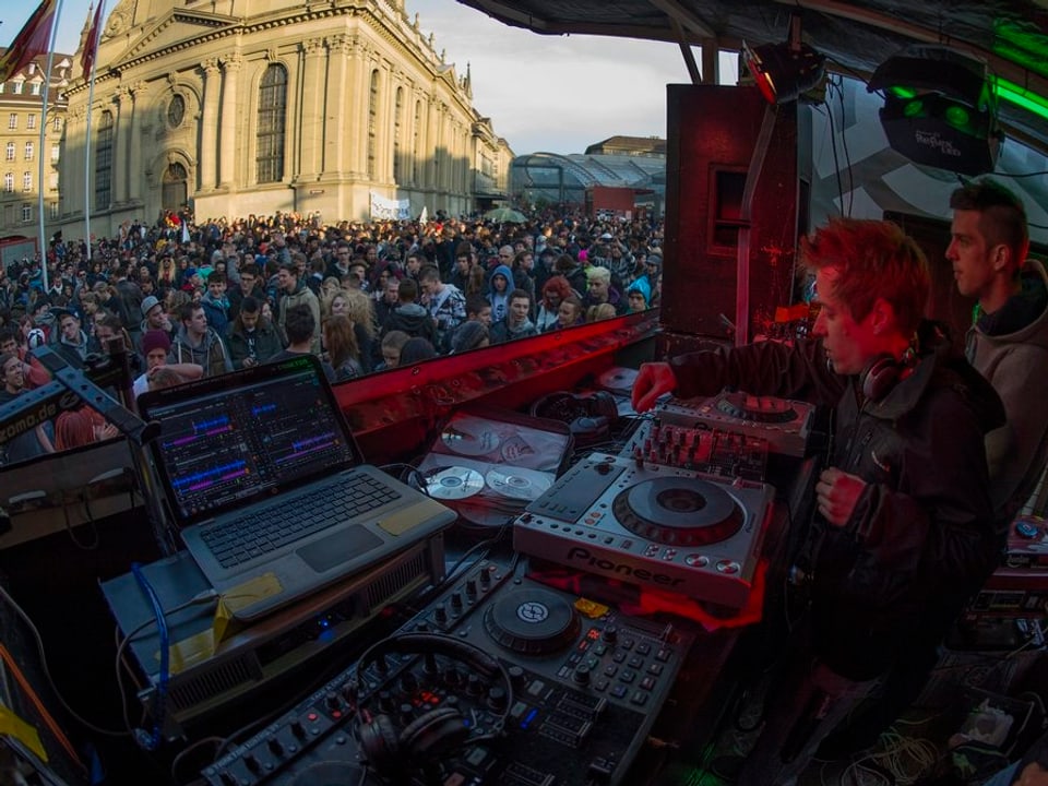 Blick über ein DJ-Pult in eine Menschenmenge