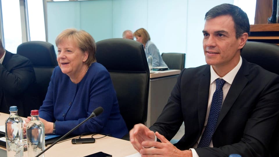 Merkel und Sanchez sitzen an einem Tisch nebeneinander.