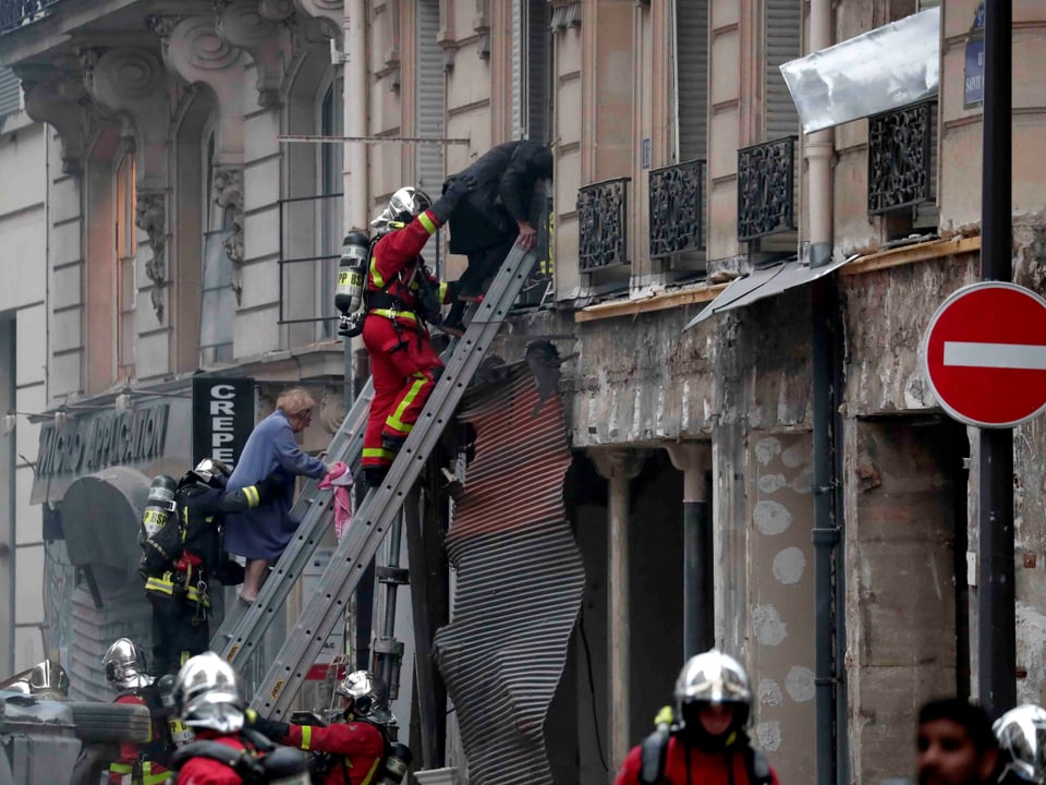 Feuerwehrmann auf einer Leiter birgt eine Person aus dem ersten Stock eines Gebäudes.