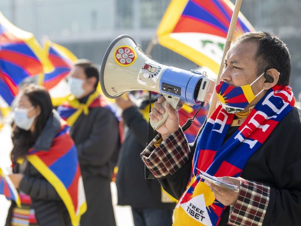 Tibeterinnen und Tibeter demonstrieren mit tibetischen Fahnen, Schals und Masken