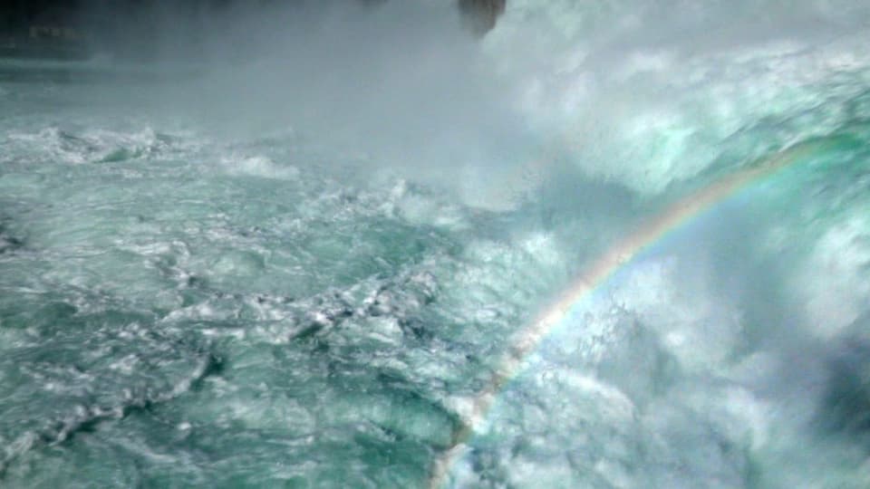 hellblau schäumendes Wasser, darüber ein Regenbogen