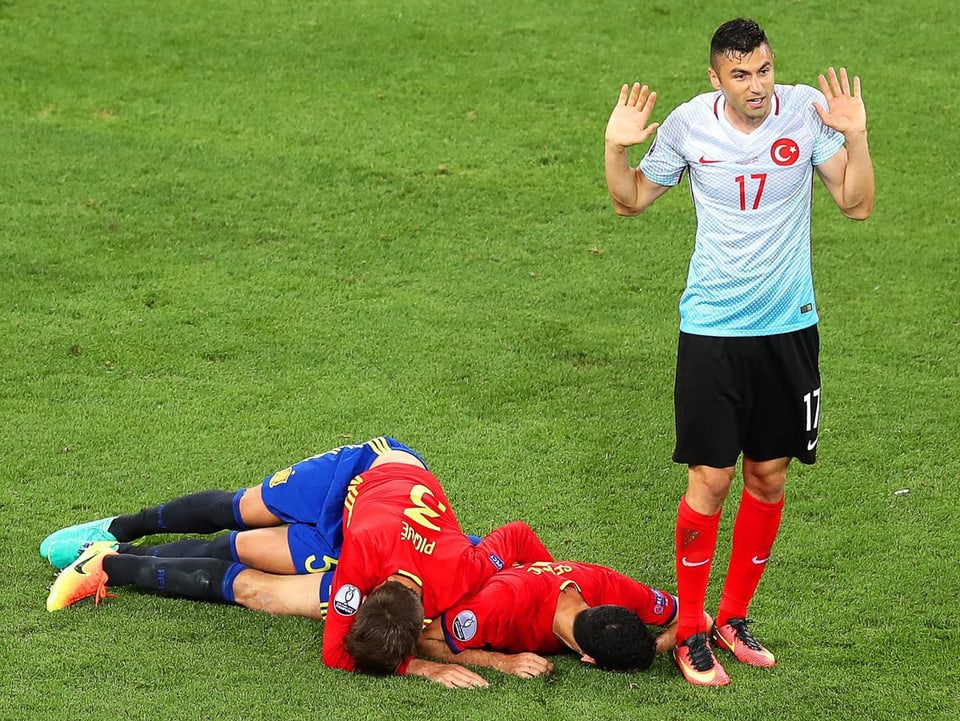 Zwei spanische Spieler am Boden, ein Türke daneben hebt, seine Unschuld beteiernd, die Hände