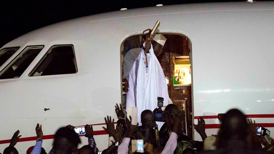 Jammeh in weissem Gewand winkt vom Eingang des Flugzeugs.